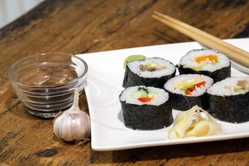 Sushi rolls on a white plate with soy sauce. Against the backdrop of a vintage wooden table.
