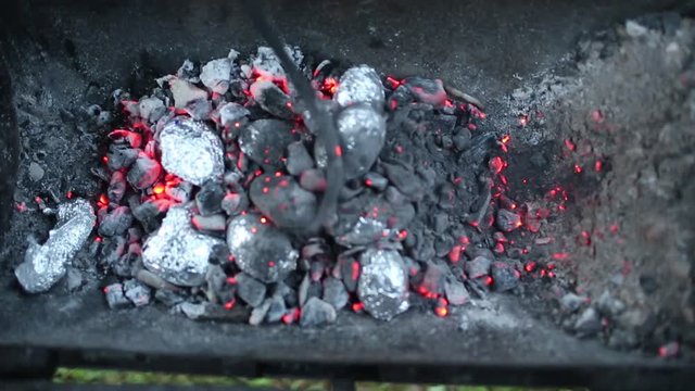 Close up of bonfire with orange and yellow flames and firewood and Baked potatoes covered with aluminum foil, Lag Baomer Jewish holiday bonfire celebration tradition of roasting Potatoes in fire