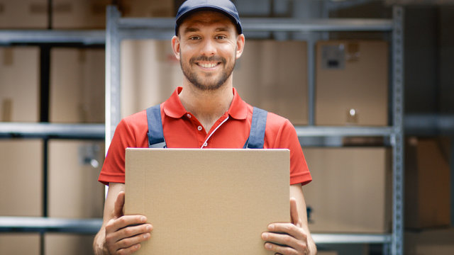 Handsome Warehouse Worker in Uniform Holds Cardboard Box Package and Smiles.