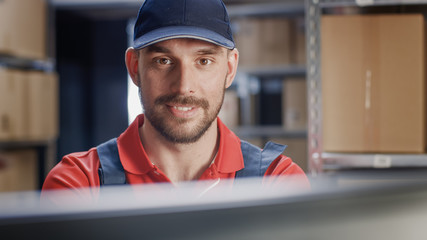 Portrait of Uniformed Worker Using Personal Computer while Sitting at His Desk in the Warehouse. 