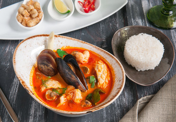 Traditional Thailand soup Tom Yam. With shrimps, mussels, scallop meat, rice and hot spices. View from above on a dark wooden background.