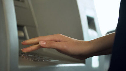 Female entering PIN number to check bank account and withdraw money from ATM