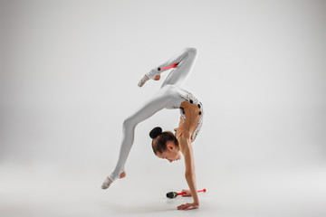 The teen female little girl doing gymnastics exercises with clubs isolated on a gray studio...