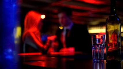 Couple first dating in nightclub, both drinking beverages, blurred background