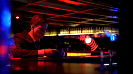 Lonely man bored at bar counter, browsing social media, lack of communication