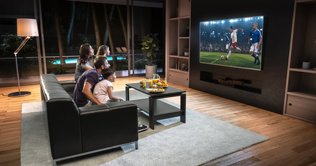A family is watching a soccer moment on the TV and celebrating a goal, sitting on the couch in the living room.