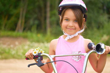 Fototapeta na wymiar Portrait of a little girl in a protective helmet controls her bike and holds a bouquet of daisies.
