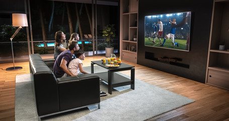 A family is watching a soccer moment on the TV and celebrating a goal, sitting on the couch in the living room.