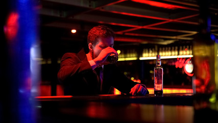 Desperate businessman drinking whiskey alone in night club, financial problems