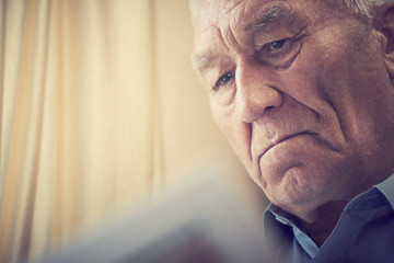 Elderly gray-haired man reading the newspaper at home. Tinted photo.