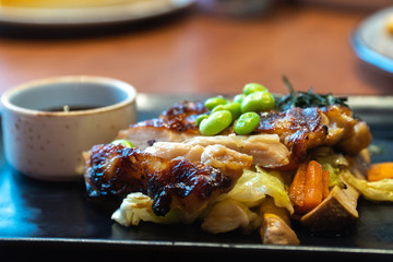close up of chicken steaks with cup of sauce on the black plate. Green peas and Japanese seaweed on chicken steaks with white cabbage, carrots and mushrooms in the restaurant