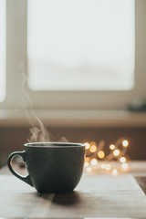Hot cup of tea or coffee. Cup with steam on the table. Warm lights in the background. vertical photo