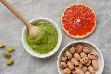 Still life of healthy food, pistachio paste, peeled and unpeeled salted pistachios, grapefruit, wooden spoon on a light background. Components for cooking.