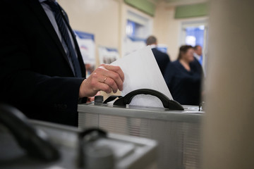 Hand of a person casting a ballot at a polling station during voting.