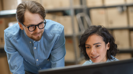 Male and Female Warehouse Inventory Managers Talking, Using Personal Computer and Checking Stock....