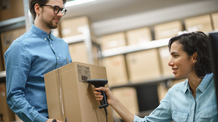 Female Inventory Manager Scans Cardboard Box and Digital Tablet with Barcode Scanner, Male Worker...
