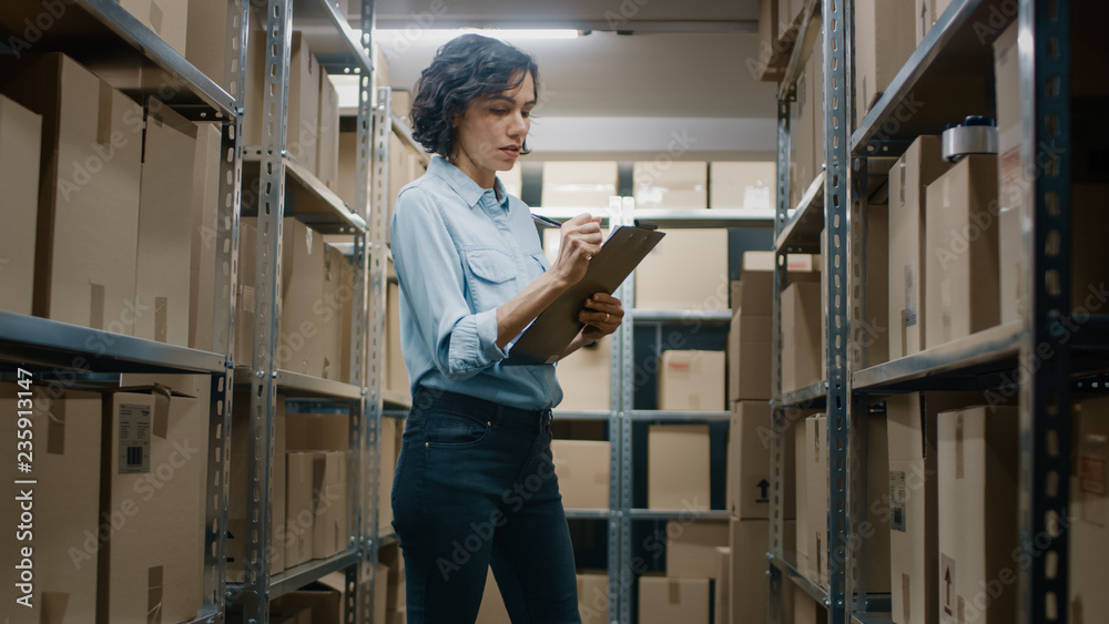 Wall mural female inventory manager checks stock, writing in the clipboard. beautiful woman working in a wareho