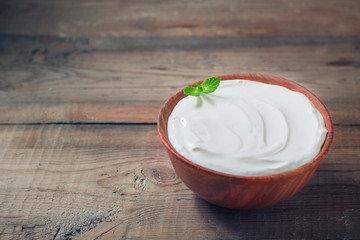 Greek yogurt in a wooden bowl on a rustic wooden table.