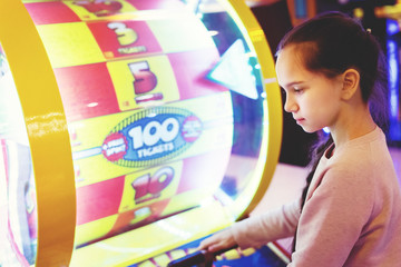 Young pretty girl with a pigtail smiles plays in the slot machine. Joyfull weekend. Fun in the game.