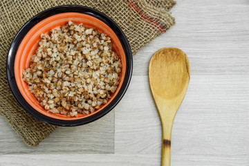 Buckwheat porridge in a plate on a light gray wooden background. View from above.