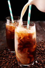 Ice coffee on a rustic table with cream being poured into it showing the texture and refreshing look of the drink