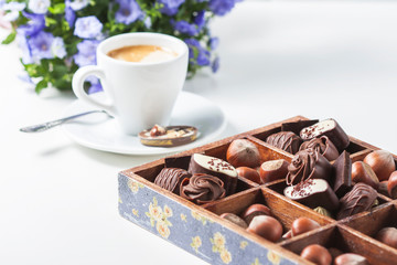 Cup of coffee on a white background with a variety of chocolates in a wooden box.
