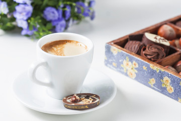Cup of coffee on a white background with a variety of chocolates in a wooden box.