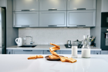 A glass of milk and toast on a table, kitchen background.
