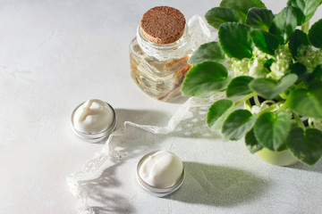 cosmetic cream with flowers on a light stone background.