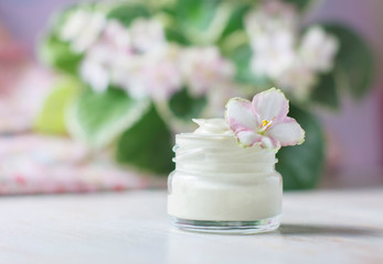 cosmetic cream with flowers on a light stone background.