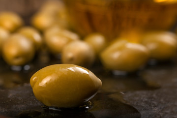 A close-up shot of olive with olives and olive oil in the background