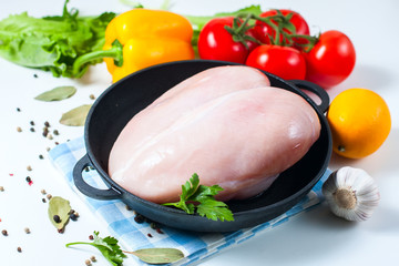 Raw chicken fillet in a cast iron frying pan with vegetables on a table, isolated on white