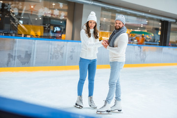 smiling couple in knitted hats and sweaters on skating rink