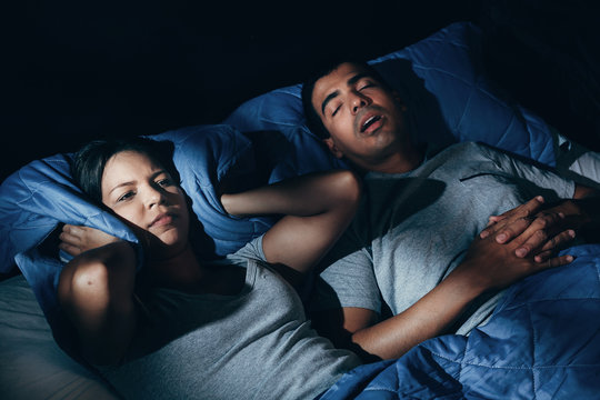 Annoyed Woman Lying In Bed With Snoring Boyfriend At Home In The Bedroom