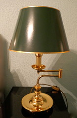 Swivel brass table lamp, light, reading lamp with dark green lampshade, in front of a light wall.
