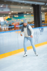 bearded man in knitted hat and sweater skating on ice rink