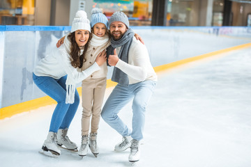 smiling parents and daughter in sweaters looking at camera on skating rink - obrazy, fototapety, plakaty
