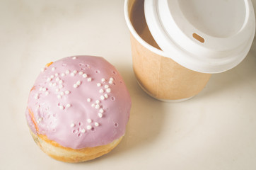 donut in glaze and a paper coffee cup/donut in glaze and a paper coffee cup on a white table. Close up