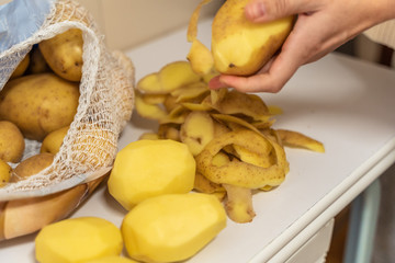 Womans hands with small kitchen knife. Potatoes peeling. Bag with unpeeled potatoes.