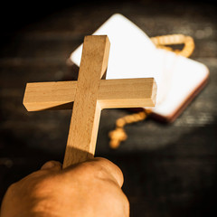 The cross held in the hand against the background of the book with the rosary