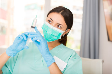 Girl nurse in mask holding syringe for injection in clinic