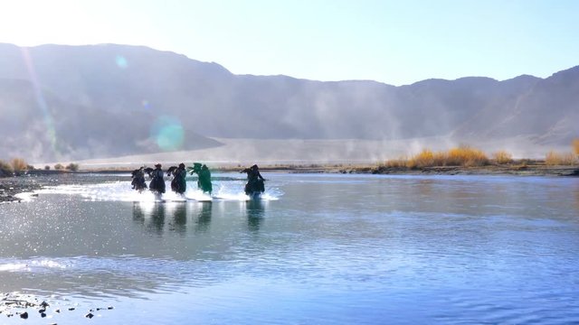 Silhouette scene of Mongolian Horsemen in the tradition clothing with the well trained hunter eagle on their arm riding horseback in the river