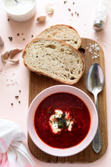 Red borscht soup in pink bowl with sour cream, bread, garlic and spices on pink background. Top view. Flat lay