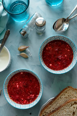 Red borscht soup in blue bowl with sour cream, bread, garlic and spices on blue wooden background. Top view. Flat lay