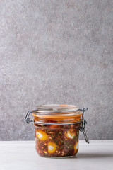 Jar with homemade pickled marinated quail eggs in tomato and olive oil sauce with anchovies and fresh parsley on white marble kitchen table. Copy space