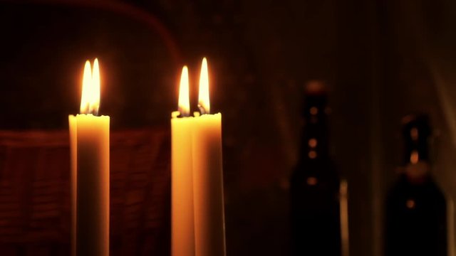 Christmas feeling with candles. Close up on burning candles moving slowly in a circle. In background a basket and some bottles. Soft and star filters used in shooting.
