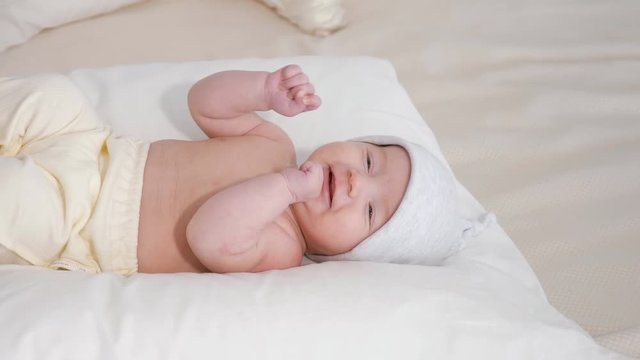 smiling baby in hat while lying on white soft bed at home.