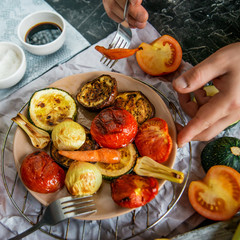Healthy and healthy food: grilled vegetables and men's hand with fork in the frame, zucchini, eggplant, tomato, onion cooked on fire, on a dark background