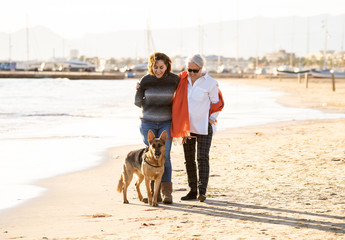 Beautiful older mom and mature daughter walking their german shepard dog on beach at autumn sunset
