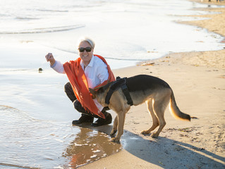 Happy attractive senior woman with her german shepard dog playing on the beach at autumn sunset